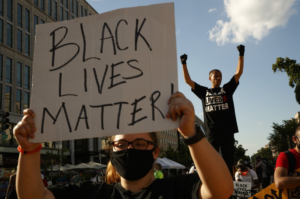 FILE - In this June 24, 2020, file photo, Antonio Mingo, right, holds his fists in the air as demonstrators protest in front of a police line on a section of 16th Street that's been renamed Black Lives Matter Plaza, in Washington. Thousands of Black activists from across the U.S. will hold the 2020 Black National Convention on Aug. 28, 2020, via livestream to produce a new political agenda that builds on the protests that followed George Floyd’s death. Organizers of the gathering shared their plans with The Associated Press on Wednesday, July 1, ahead of an official announcement. (AP Photo/Jacquelyn Martin, File)