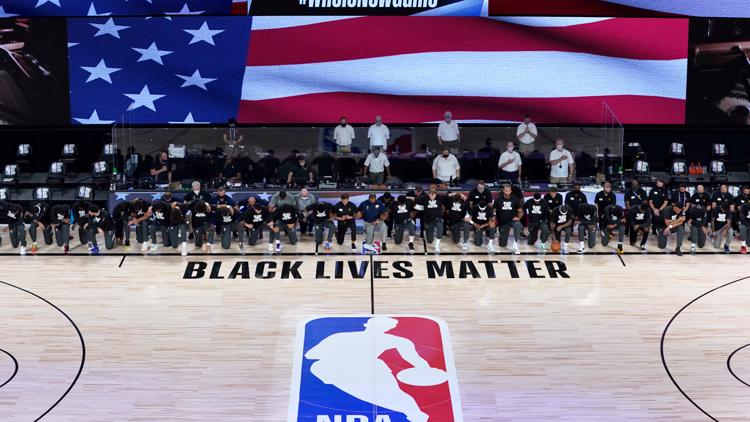 Members of the New Orleans Pelicans and Utah Jazz kneel together around the Black Lives Matter logo on the court during the national anthem before the start of an NBA basketball game Thursday, July 30, 2020, in Lake Buena Vista, Fla. (AP Photo/Ashley Landis, Pool)