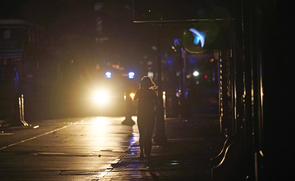 A police officer patrols past woman walking along Bourbon Street in the French Quarter after Hurricane Ida knocked out power to the city, Monday, Aug. 30, 2021, in New Orleans, La. (AP Photo/Eric Gay)